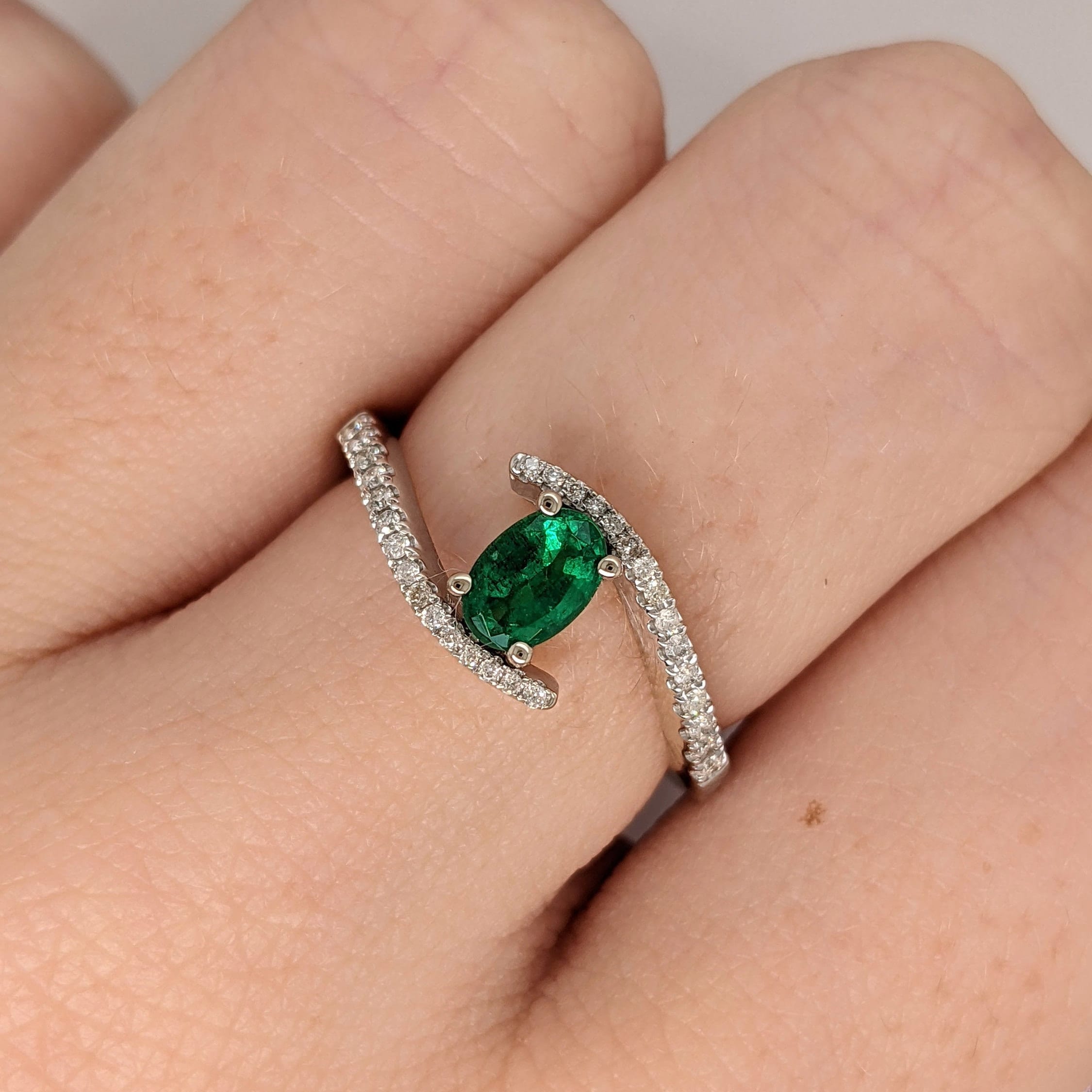This NNJ Designs Pine Green Emerald Ring in 14k White Gold and pave diamond shank is an elegant piece for any jewelry enthusiast. The oval 6x4mm gemstone is securely set in a bypass style and adorned with a pave diamond shank. Perfect for any occasion, the ring is a beautiful choice for May birthdays, anniversaries, and special occasions like Christmas. Fine Jewelry by Nancy Jain 