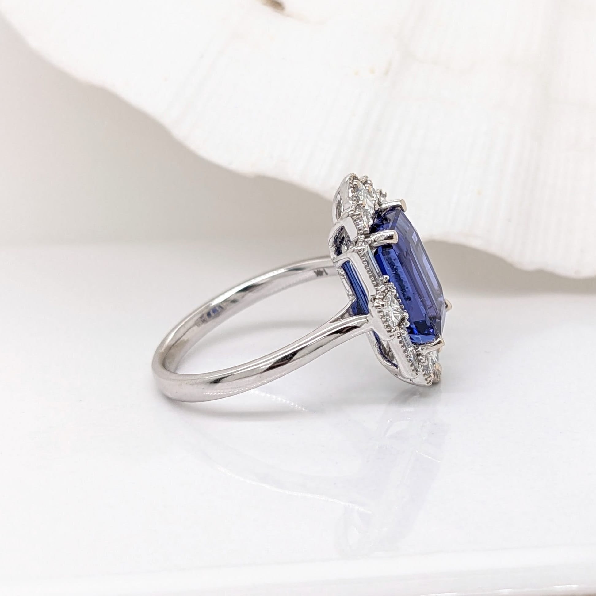 emerald cut tanzanite 9x7mm blue natural gemstone and diamond ring in 14k white gold with milgrain detail, art deco style with a straight shank and halo of 4 baguette diamond accents 4 princess diamond accents and 4 round diamond accents